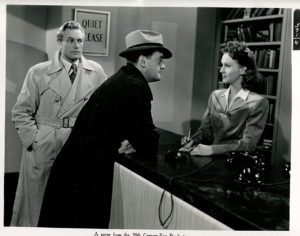 A still from noir classic "Quiet Please Murder" a librarian regards a detective and his companion askance. Her fall vintage fashion is on point. 