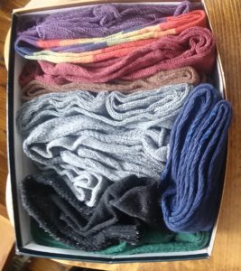 A shoe box filled with multi-colored socks.