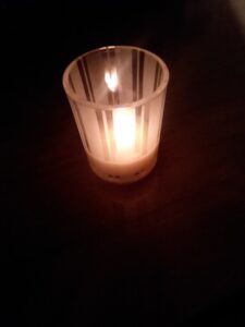 A tealight burns in a small striped glass holder, shining in the dark. 