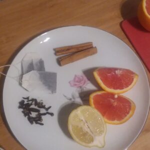 A plate with cinnamon sticks, orange and lemon segments, a small pile of cloves, and tea bags. 